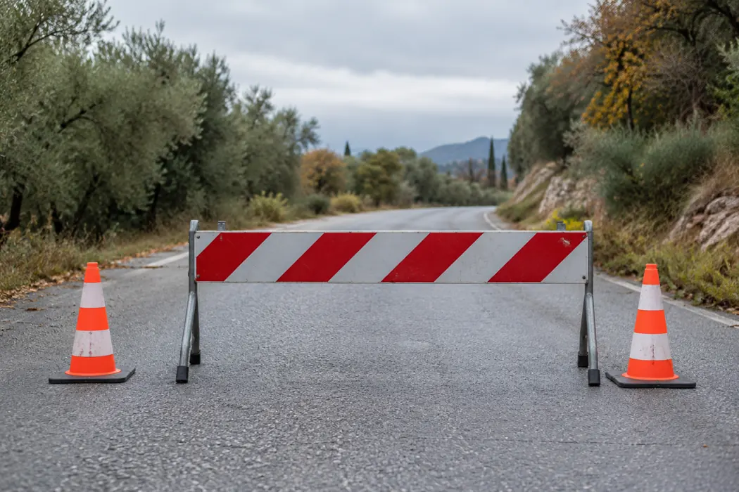 A portable red-and-white barrier and traffic cones on an empty rural road